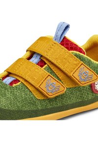 Grüner und gelber Kindersneaker mit rotem Mesh, doppeltem gelbem Klettverschluss mit kleinem blauem Vogel-Logo und einer hellblauen Textilschlaufe.