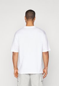 Camiseta de algodón blanca con cuello redondo y mangas cortas, que presenta un corte relajado y aberturas laterales para mayor facilidad de movimiento.