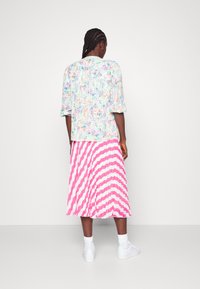 Camisa floral de mangas curtas em cores pasteis combinada com uma saia plissada em rosa e branco com riscas, acentuada com sapatilhas brancas e meias de tornozelo.