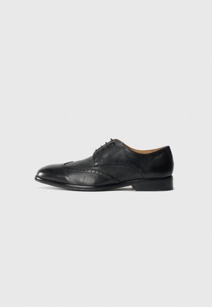 Zapato de vestir para hombre en cuero negro con detalles de brogue y cordones, mostrado en perfil derecho sobre un fondo blanco.