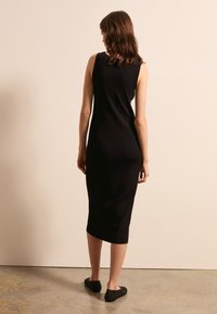 Abito midi nero senza maniche con silhouette aderente, texture liscia e colore uniforme. Indossato con scarpe slip-on nere a trama.