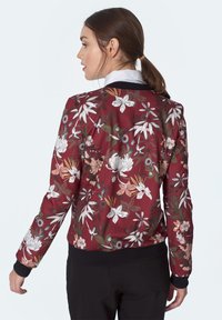 Burgundowa kurtka bomber z florystycznym wzorem w białe, różowe i zielone akcenty. Czarne ściągacze przy mankietach i u dołu. Gładka tekstura.