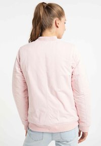 Lichtroze bomberjack met een ribbelkraag en -manchetten, met een gladde textuur en een getailleerde pasvorm. Achteraanzicht met minimale details.