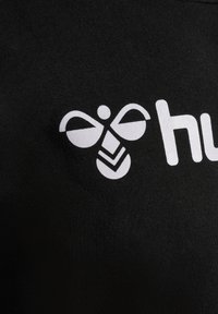 Zwarte stof met een opvallend wit logo van een gestileerde bij met vleugels en een abstract ontwerp, waarbij de nadruk ligt op duidelijkheid en contrast.