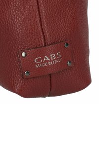Borsa in pelle rossa con texture, con un'etichetta visibile che riporta "GABS MADE IN ITALY", accentuata da viti metalliche, che mostra un design morbido ma strutturato.