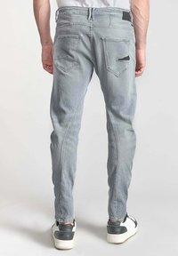 Szare dżinsy z dopasowanym krojem, z tylnymi kieszeniami, detalami na szwie bocznym oraz przetarciami nad prawą kieszenią.