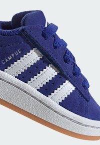Baskets en daim bleu avec design à trois bandes blanches, semelle texturée, bout rond et lacets bleus. "CAMPUS" imprimé sur le côté.