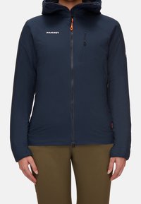 Mörkblå isolerad jacka med dragkedja framtill, justerbar huva och en bröstficka. Har orangea dragkedjedetaljer och elastiska muddar.