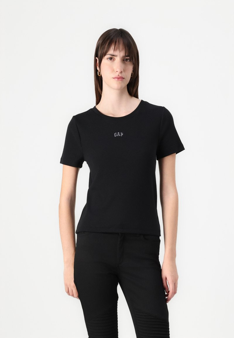 T-shirt en coton noir à manches courtes, avec un col rond et un petit logo "GAP" blanc à l'avant. Design simple et ajusté.