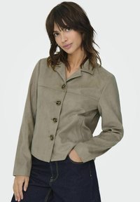 Brun mockajacka med krage, fem knappar och sidofickor. Har en något kortad design och långa ärmar.