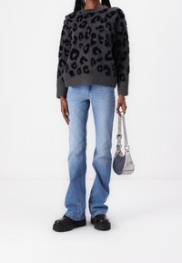 Pullover leopardato nero con dettagli testurizzati, jeans aderenti blu chiaro e scarpe nere chunky. Una borsa a spalla argento aggiunge un tocco metallico.