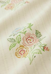 Tessuto ricamato con disegni floreali pastello in rosa, giallo e blu su uno sfondo cremoso e strutturato con righe verticali.