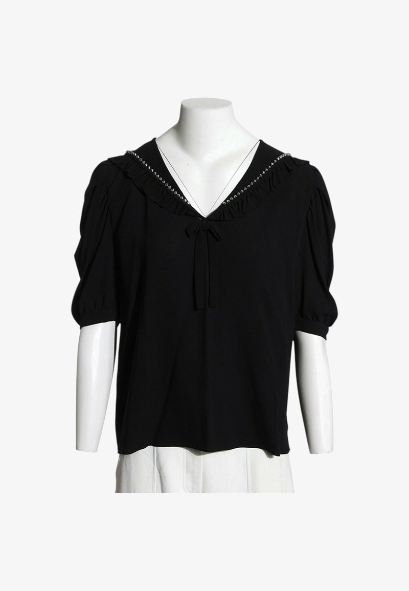 Blouse noire à manches courtes avec encolure en V froufroutante et petit nœud au centre, exposée sur un buste de mannequin blanc.