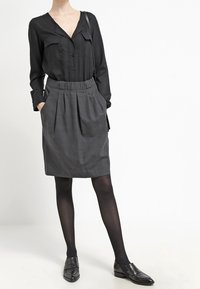 Chemise noire à manches longues avec boutons, jupe plissée grise, collants noirs et mocassins noirs. Look décontracté avec poches sur la jupe et design simple.