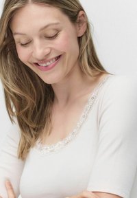 Lys beige ribbet top med korte ærmer og detaljer i bølgeformet blonde ved halsudskæringen. Blød tekstur, tætsiddende design, minimalistisk stil.