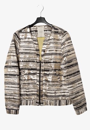 Stribet metallic sølv og beige lynlåsjakke med sorte vandrette linjer, hængende på en sort bøjle.