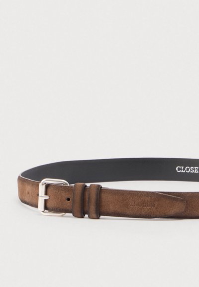 Καφέ σουέντ ζώνη με ασημένια αγκράφα και δύο θηλιές, μερικώς τυλιγμένη σε ανοιχτό γκρι φόντο.