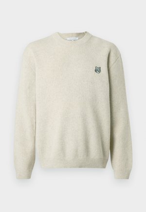 Krém színű pulóver, puha anyagból, bordás kerek nyakkal, hosszú ujjal és egy kis hímzett farkaskészlettel a mellrészen.