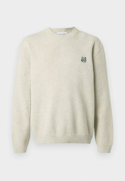 Krēmkrāsas džemperis, izgatavots no mīksta auduma, ar ribotu apkakli, garām piedurknēm un mazu izšūtu vilku detaļu uz krūtīm.