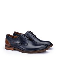 Chaussures en cuir bleu marine avec une finition lisse, des accents brun clair, un panneau latéral texturé et un bout arrondi. Présente un système de laçage et une semelle en caoutchouc.