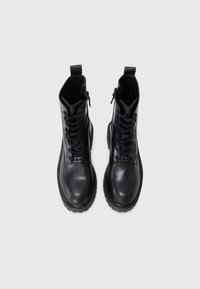 Bottines en cuir noir avec un laçage à l'avant, fermeture éclair sur le côté et semelle en caoutchouc texturé. Caractéristiques d'une finition lisse et d'une conception robuste.