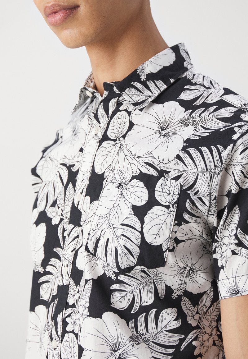 Korte mouwen shirt van zwarte katoen met een witte bloemenprint van hibiscus en bladpatronen, met een knoopsluiting bij de kraag en een borstzakdetail.