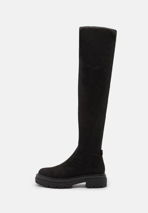 Bottes en suède noir, au-dessus du genou, avec un bout rond, une semelle en caoutchouc épaisse et un design minimaliste. Texture lisse et pas de matériel visible.