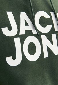 Grüne Kapuzenjacke aus weichem Stoff mit großen weißen Buchstaben "JACK & JONES" auf der Vorderseite, mit einer Kängurutasche und Kordeln.