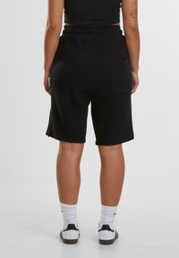 Svarta ribbade stickade shorts med elastisk midja, som har en bakficka och upprullade fållar, ihopparade med vita strumpor och skor.