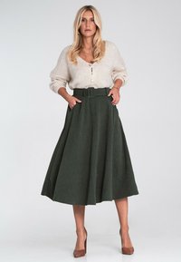 Zielona, plisowana spódnica midi z szerokim paskiem i kieszeniami, w połączeniu z kremowym, teksturowanym kardiganem. Brązowe obcasy uzupełniają cały strój.