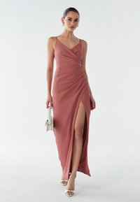 Maksi kleita dusaini rozā krāsā ar drapētu dizainu, dziļu sānu šķēlumu, regulējamiem siksniņām un gludu tekstūru. Saskaņota ar mazu baltu somiņu.