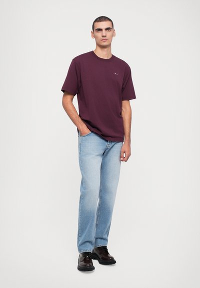 Camiseta de algodón burdeos, corte holgado, mangas cortas. Vaqueros rectos de azul claro. Zapatos de cuero oscuros. Diseño sencillo, sin patrones ni acentos visibles.