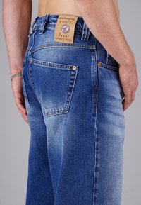 Blaue Denim-Jeans mit geradem Schnitt, verwaschenem Stoff, zwei Gesäßtaschen und einem hellbraunen Leder-Logo am Bund.