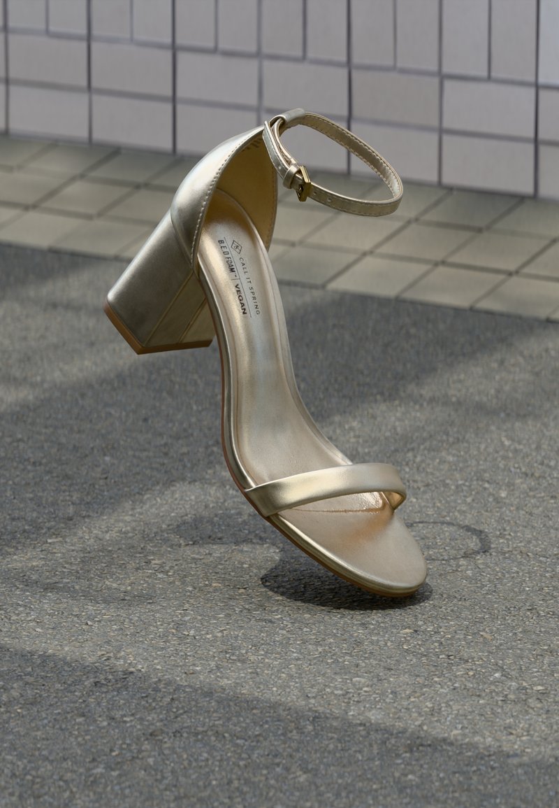 Χρυσό vegan δερμάτινο πέδιλο με τακούνι block, λουράκι αστραγάλου και μινιμαλιστικά λουράκια επάνω στο πόδι. Λεία υφή και γυαλιστερό φινίρισμα.