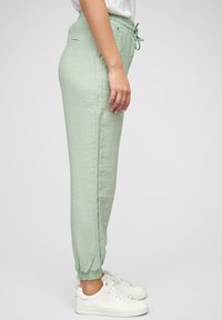 Jogging en vert clair avec une taille élastique et un cordon de serrage. Comprend des poches latérales et des poignets élastiques. Fabriqué en tissu doux et texturé.