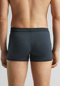 Boxers de color gris oscuro con una tela texturizada, que cuentan con una cinturilla elástica negra, ajustándose de manera ceñida y llegando hasta la mitad del muslo.
