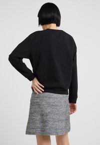 Felpa nera con maniche lunghe e polsi a costine, abbinata a una gonna grigia texturizzata. Design semplice e rilassato senza hardware o motivi visibili.