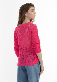 Stickad tröja i stark rosa med ett mönster i diamantspets, långa ärmar och ribbade muddar. Lättviktig med en öppen, luftig design.