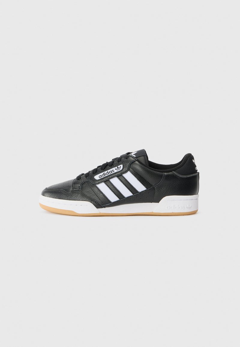 Sneaker de couro preto com três riscas brancas, frente com atacadores e sola em borracha de goma. Apresenta um cabedal texturizado e detalhes de marca.