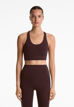 Bordeaux sportbeha met een ronde halslijn en brede banden, gecombineerd met hoge taille leggings met een gebogen naaddetail.