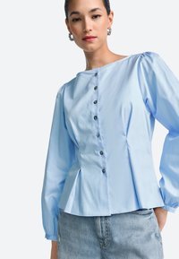 Light blue button-up blouse with puff sleeves, a straight neckline, and a peplum waist, featuring small, dark buttons along the front.