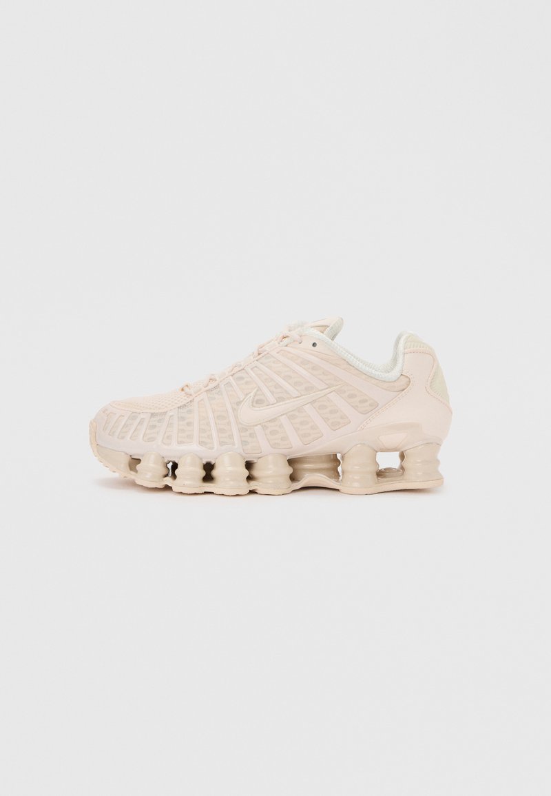 Μπεζ αθλητικό παπούτσι Nike Shox με χαρακτηριστικές ελατηριωτές στήλες απορρόφησης στην σόλα, επάνω μέρος από δίχτυ και λογότυπο Nike swoosh στο πλάι.