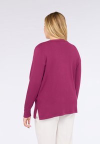 Magenta pletený svetr s dlouhými rukávy, kulatým výstřihem a postranními rozparky, vyrobený z měkkého materiálu, vystavený zezadu.