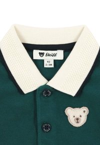 Dark green polo shirt featuring a cream knitted collar with navy accents, a bear logo patch, and black buttons. Size label 62, 2-3M.