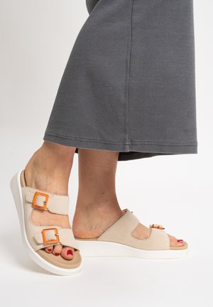 Beige Sandalen mit zwei Schnallenriemen und orangefarbenen Akzenten, ausgestattet mit einer weißen Plateau-Sohle. Das Obermaterial besteht aus weichem Stoff mit Ausschnittdetails.