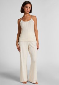 Σετ πυτζάμας σε κρεμ χρώμα με ριμπ ύφανση, που περιλαμβάνει ένα καμισόλ με δαντελένιο τελείωμα και παντελόνια με φαρδιά πατλάκια διακοσμημένα με μικρές ροζ λεπτομέρειες.