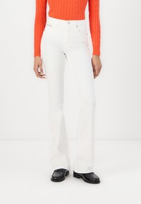 Vaqueros blancos acampanados con cintura alta y bolsillos, combinados con un suéter de canalé naranja. El calzado son mocasines negros tejidos.