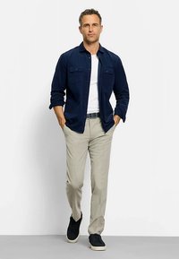 Marineblaues Langarmshirt mit Knopftaschen, weißes T-Shirt, beige Hose und schwarze Sneaker. Glatter Stoff mit entspannter Passform und lässigem Design.