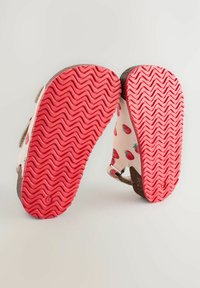 Weiße Sandalen mit einem Erdbeermuster und strukturierten rosa Gummisohlen. Verfügen über verstellbare Riemen und ein braunes Akzentdetail an der Ferse.