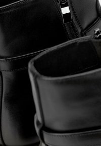 Botas de cuero negro con una textura suave, doble correa y cremallera lateral. El interior está forrado con un material suave para mayor comodidad.